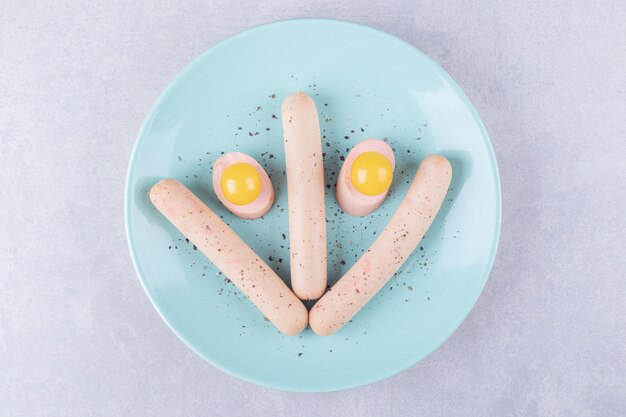 Salsicce bollite e tuorlo d'uovo sul piatto blu.