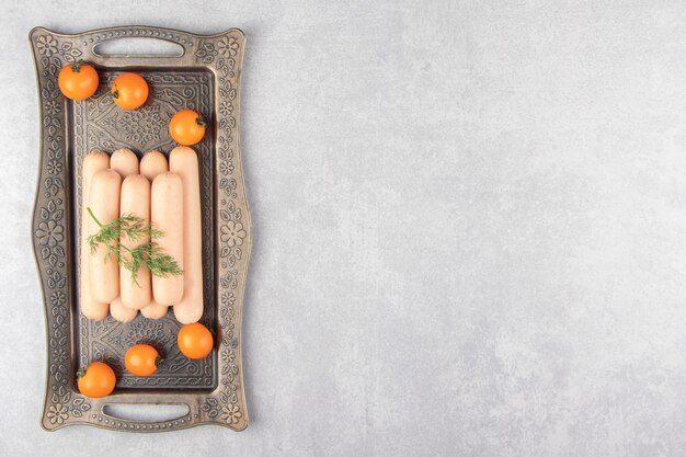 Salsicce bollite fresche e pomodorini sul vassoio.