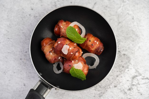 Salsiccia avvolta nella pancetta di maiale in una padella.