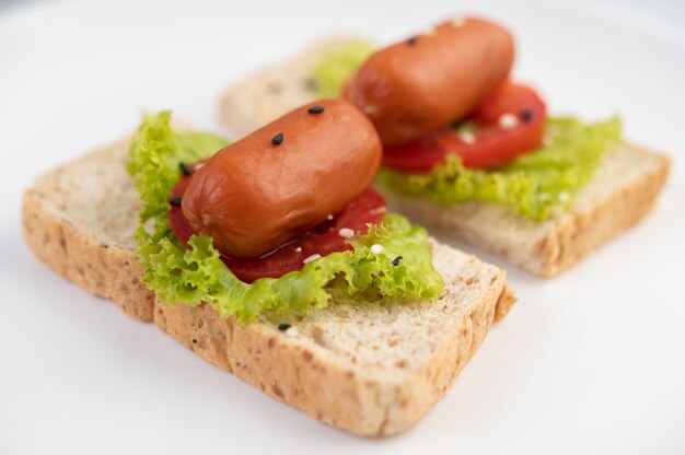 Salsiccia con pomodori, insalata e due set di pane su un piatto bianco.