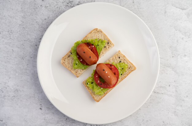 Salsiccia con pomodori, insalata e due set di pane su un piatto bianco.