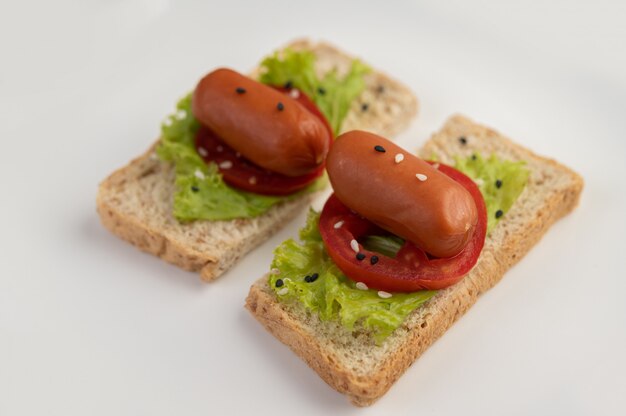 Salsiccia con pomodori, insalata e due set di pane su un piatto bianco.