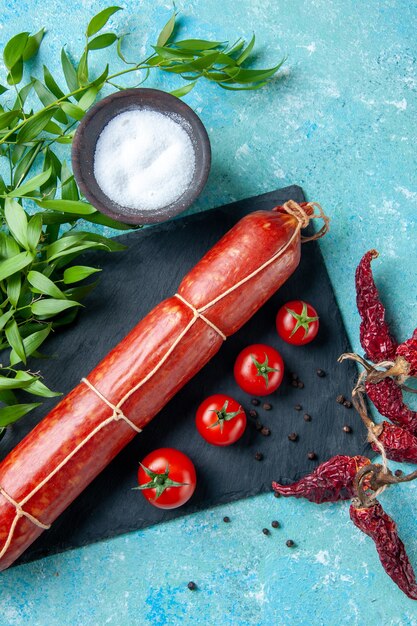 Salsiccia gustosa vista dall'alto con pomodori rossi su sfondo azzurro colore cibo hamburger farina pane a base di carne