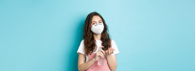 Salute coronavirus e concetto di allontanamento sociale La giovane donna nel respiratore pulisce le mani dai germi usando un disinfettante per le mani applica l'antisettico su sfondo blu palma