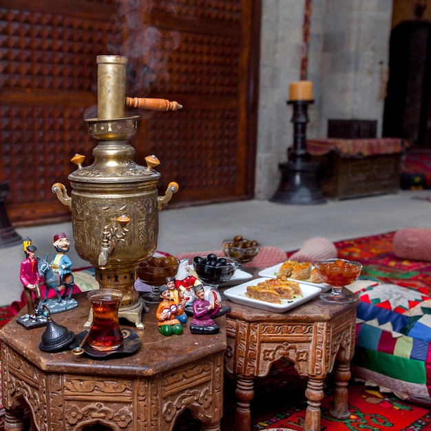 Samovar di vista laterale con bicchiere di tè e figurine e baklava in tavola sul ristorante