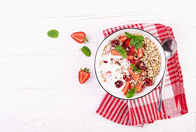 Sana colazione - muesli, fragole, ciliegia, noci e yogurt in una ciotola su un tavolo di legno. Concetto di cibo vegetariano. Vista dall'alto