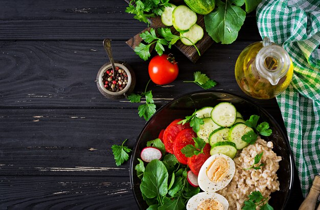 Sana insalata di verdure fresche - pomodori, cetrioli, ravanelli, uova, rucola e farina d'avena sulla ciotola. Dieta alimentare. Disteso. Vista dall'alto