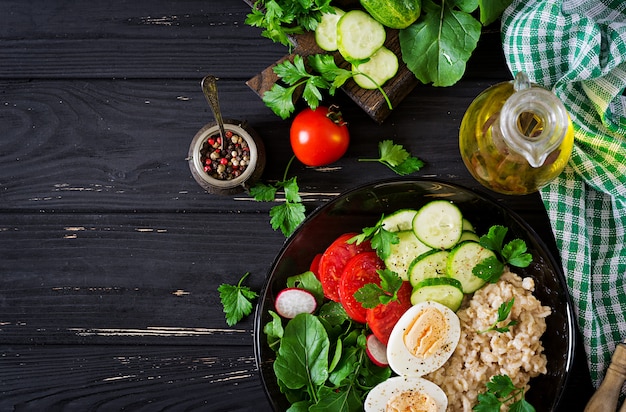 Sana insalata di verdure fresche - pomodori, cetrioli, ravanelli, uova, rucola e farina d'avena sulla ciotola. Dieta alimentare. Disteso. Vista dall'alto