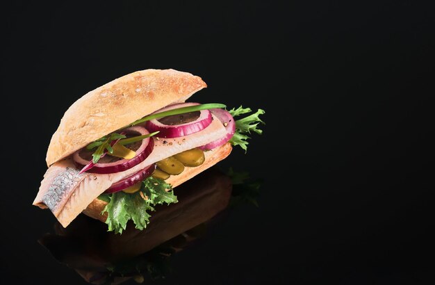 Sandwich olandese con aringhe e sottaceti cetriolo sottaceto e cipolla rossa sul tavolo a specchio scuro. Primo piano, messa a fuoco selettiva e spazio di copia