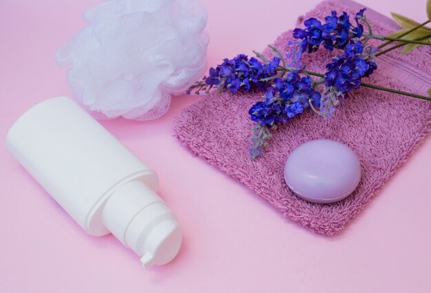 Sapone; asciugamano; fiore di lavanda; Luffa e bottiglia cosmetica su sfondo rosa