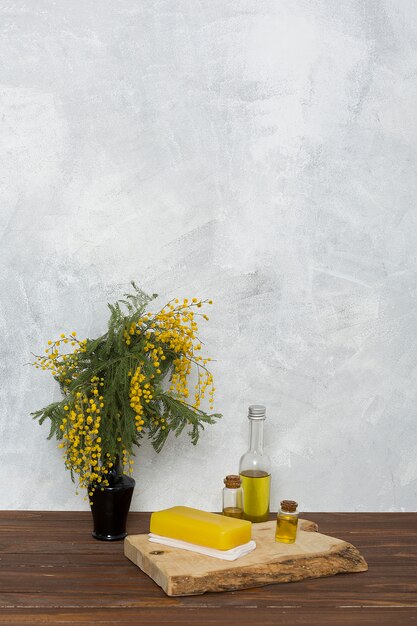 Sapone di erbe giallo sul tovagliolo piegato e bottiglia di olio essenziale vicino al vaso di fiori giallo mimosa