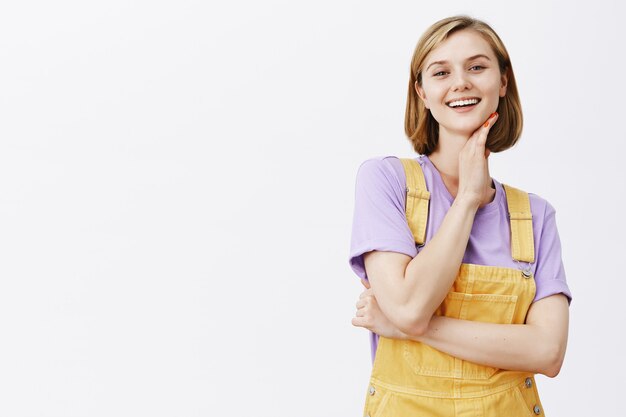 Sassy bella giovane studentessa sorridente, toccando il viso con sguardo soddisfatto