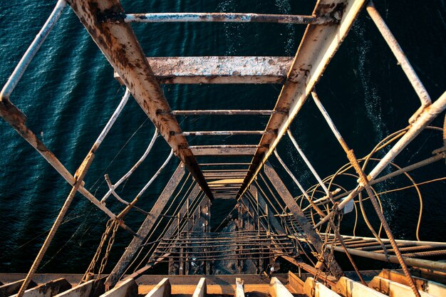 Scala estremamente vecchia e squarciata che scende verso il mare ondulato a partire da un vecchio ponte