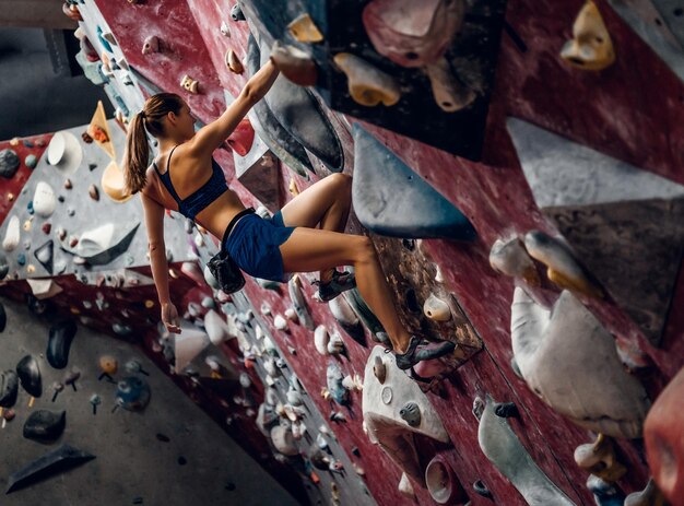 Scalatore professionista femminile su una parete di bouldering all'interno.