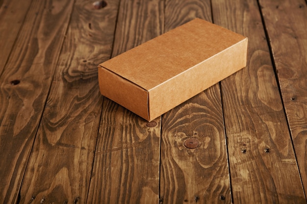 Scatola di cartone chiusa del pacchetto presentata sulla tavola di legno spazzolata sollecitata, vista laterale, isolata sul centro