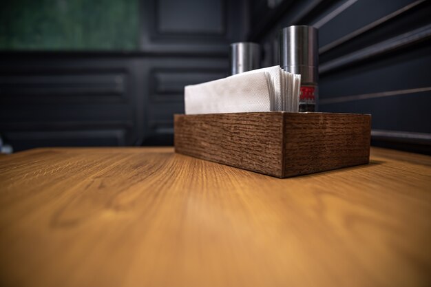 Scatola di legno con spezie e tovaglioli su un tavolo in un bar, primo piano.