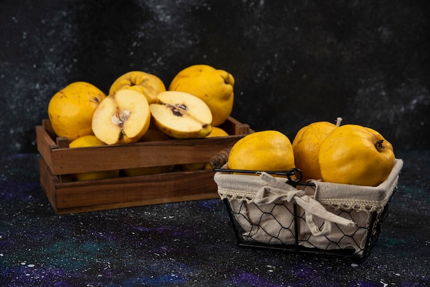 Scatola di legno e cesto di mele cotogne fresche mature sul tavolo scuro.