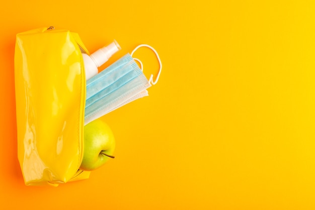 Scatola di penna gialla vista dall'alto con mela spray e maschera sulla superficie arancione