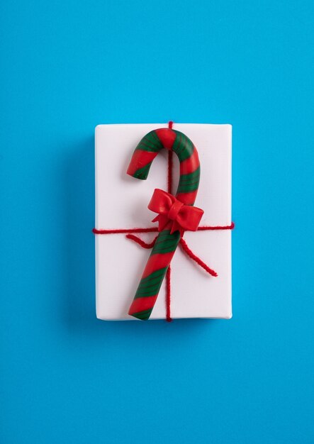 Scatola regalo natalizia bianca decorata con un bastoncino di zucchero sulla superficie blu