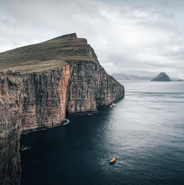 Scatto che cattura la splendida natura delle Isole Faroe, una barca che galleggia nel mare vicino alle scogliere