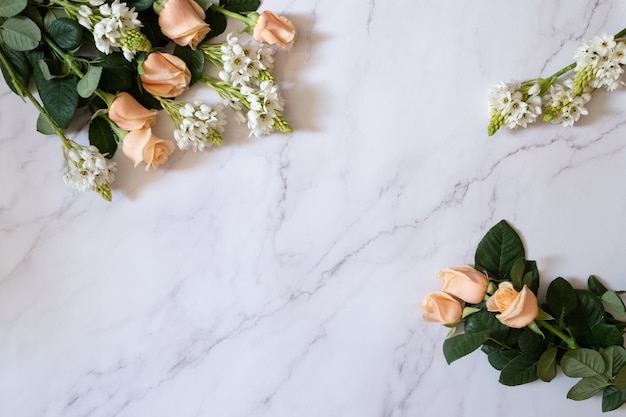 Scatto dall'alto di rose da giardino con foglie verdi e piccoli fiori bianchi su una superficie di marmo bianco