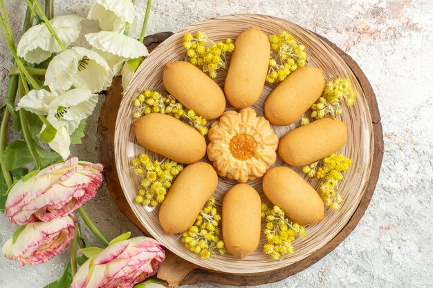 Scatto dall'alto di un piatto di biscotti su un piatto di legno e fiori bianchi e rosa su fondo di marmo