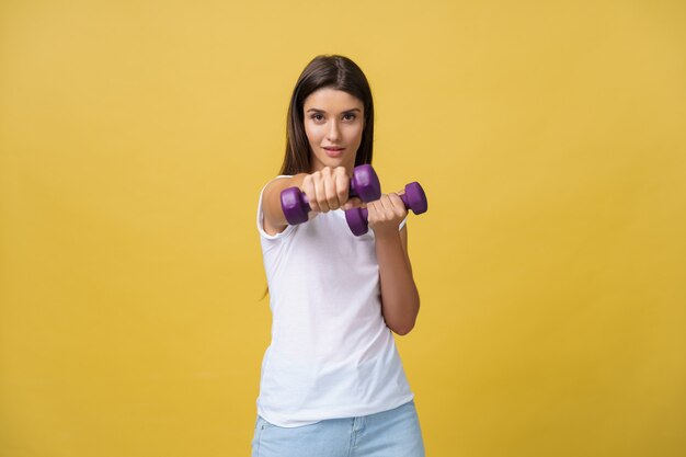 Scatto di una giovane donna bella e sportiva che solleva pesi su sfondo giallo.