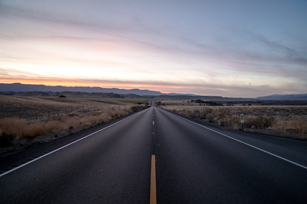 Scatto di una strada autostradale circondata da campi di erba secca sotto un cielo durante il tramonto