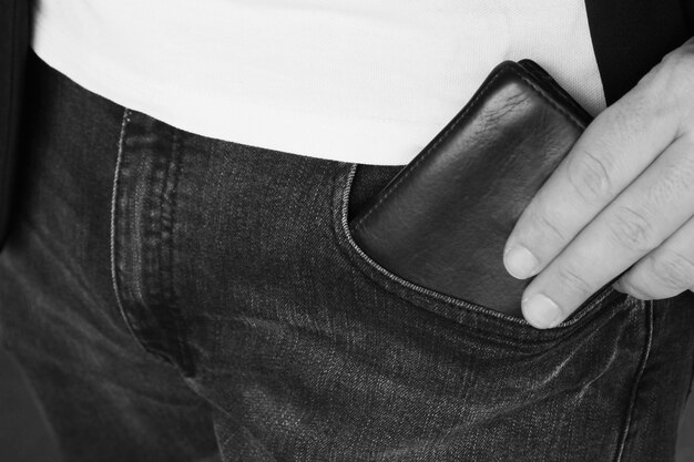 Scatto in scala di grigi di una persona che mette un portafoglio in pelle in tasca