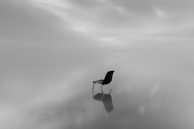 Scatto in scala di grigi di una sedia su una superficie d'acqua con una riflessione in una giornata piovosa
