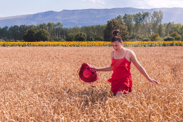 Scatto ipnotizzante di una donna attraente con un vestito rosso in posa davanti alla telecamera in un campo di grano