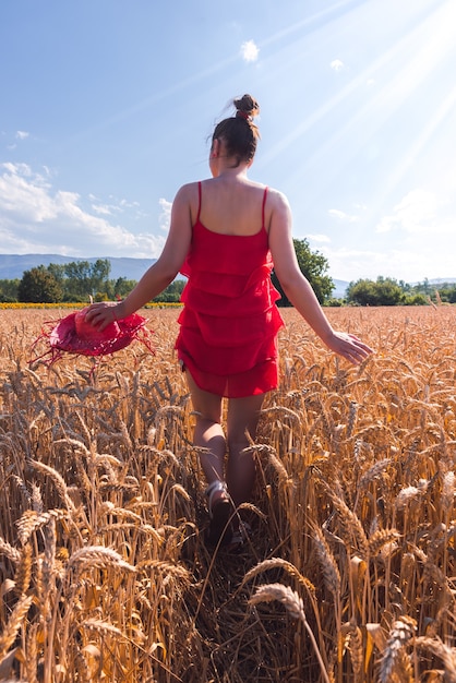 Scatto ipnotizzante di una donna attraente con un vestito rosso in posa davanti alla telecamera in un campo di grano