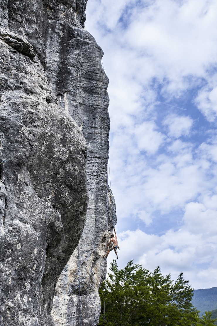 Foto gratuito scatto mozzafiato di un giovane maschio che si arrampica sull'alta roccia a champfromier, francia