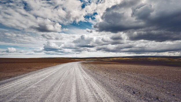 Scatto mozzafiato di una strada isolata che si estende attraverso un bellissimo campo sotto il cielo nuvoloso