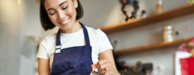 Scatto verticale di una ragazza bruna asiatica barista che indossa un grembiule che prepara il caffè che prepara l'ordine nel caffè