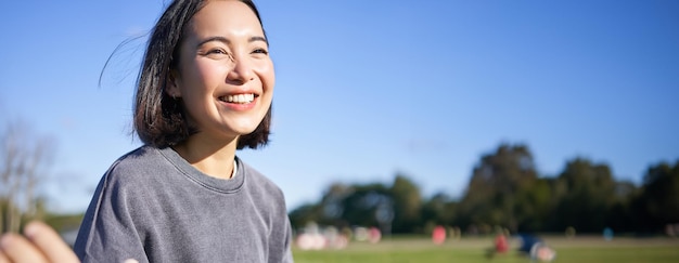 Scatto verticale di una ragazza coreana felice seduta nel parco che impara a suonare l'ukulele cantando e rilassandosi