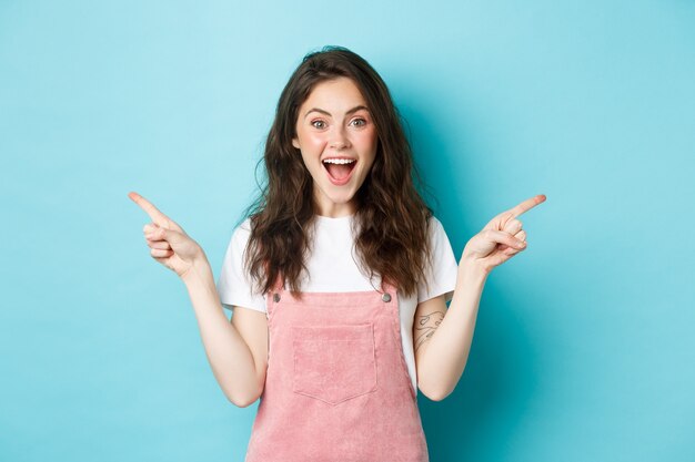 Scegli la tua parte. Sorridente donna eccitata che urla di gioia, puntando le dita lateralmente nello spazio della copia sinistra e destra, mostrando un buon affare pubblicitario, in piedi su sfondo blu.