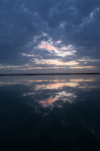 Scenario mozzafiato del cielo al tramonto con nuvole temporalesche che si riflettono sulla superficie dell'acqua