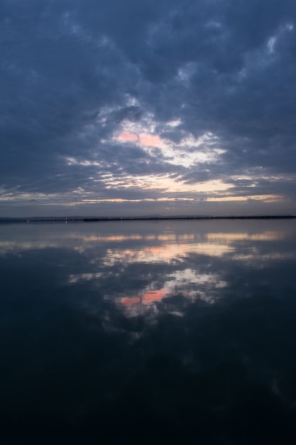 Scenario mozzafiato del cielo al tramonto con nuvole temporalesche che si riflettono sulla superficie dell'acqua