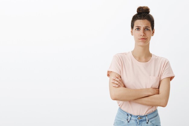 Scettico attraente giovane donna elegante in posa contro il muro bianco