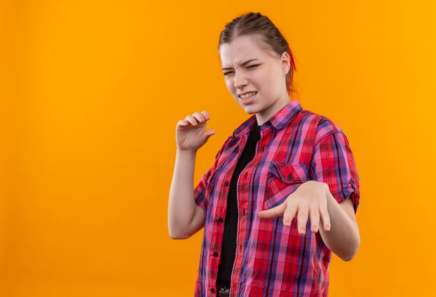 Schizzinosa giovane bella ragazza che indossa la camicia rossa tendendo la mano alla fotocamera su sfondo giallo isolato con spazio di copia