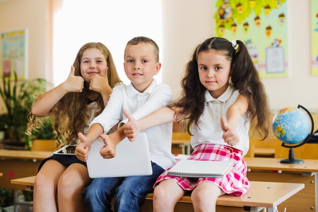 Schoolkids seduto sulla scrivania dando pollice in su