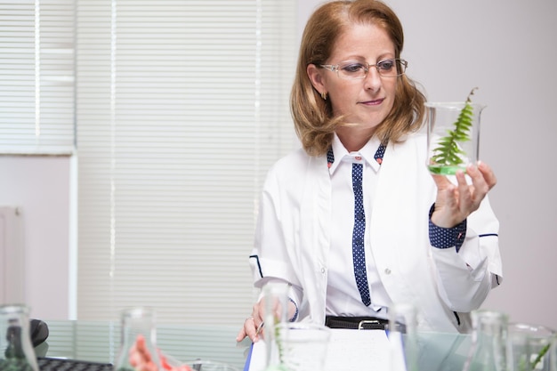 Scienziata che controlla la pianta dopo aver fatto un test di biologia su di essa. Laboratorio di chimica. Prova scientifica.