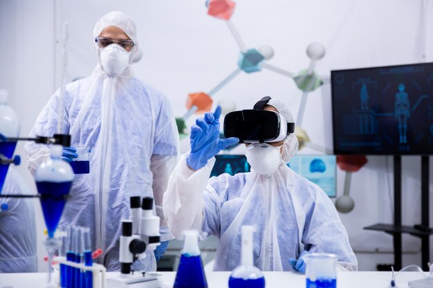 Scienziata che lavora con occhiali per realtà virtuale nel laboratorio di ricerca con il suo assistente in background.