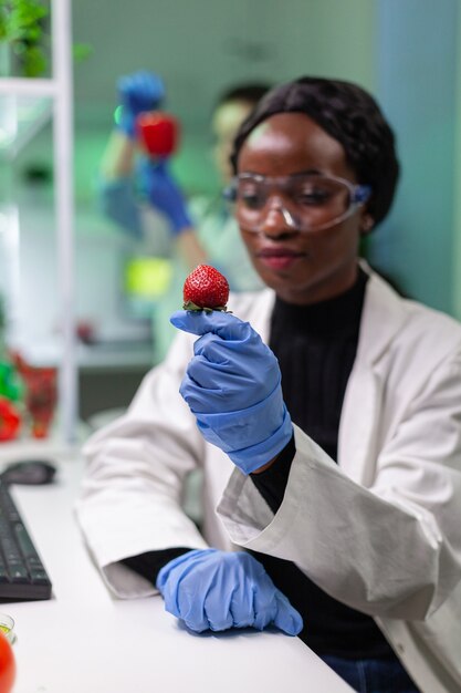 Scienziato chimico guardando la fragola con liquido organico esaminando il test del DNA dei frutti per esperimenti di botanica