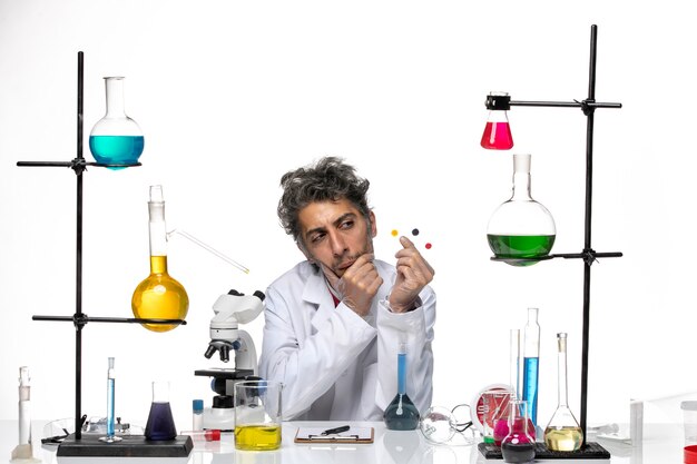 Scienziato maschio di vista frontale che tiene campioni davanti al tavolo con soluzioni su sfondo bianco coronavirus health lab covid