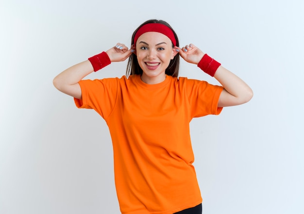 Sciocca giovane donna sportiva indossando la fascia e braccialetti sorridenti che fanno grandi orecchie isolate