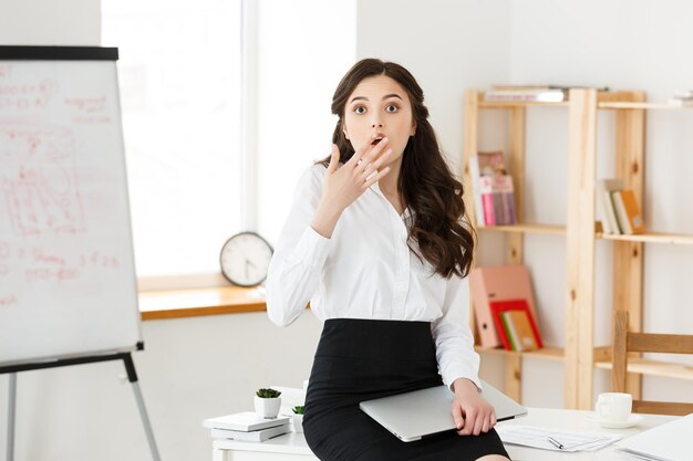 Scioccata giovane donna d'affari sorpresa con qualcosa davanti seduto in un ufficio moderno