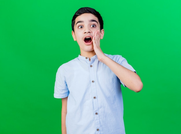 Scioccato giovane ragazzo caucasico guardando il lato tenendo la mano sul viso isolato sulla parete verde con lo spazio della copia