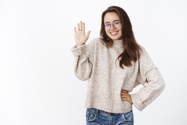 Sciocco, piacevole e carismatica giovane donna con gli occhiali e il maglione che flirta e ride carina come alzando la mano